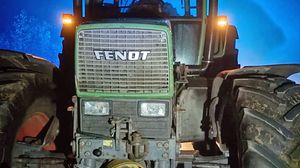 Traktor marki Fendt stojący na drodze w nocy, oświetlony niebieskim światłem.