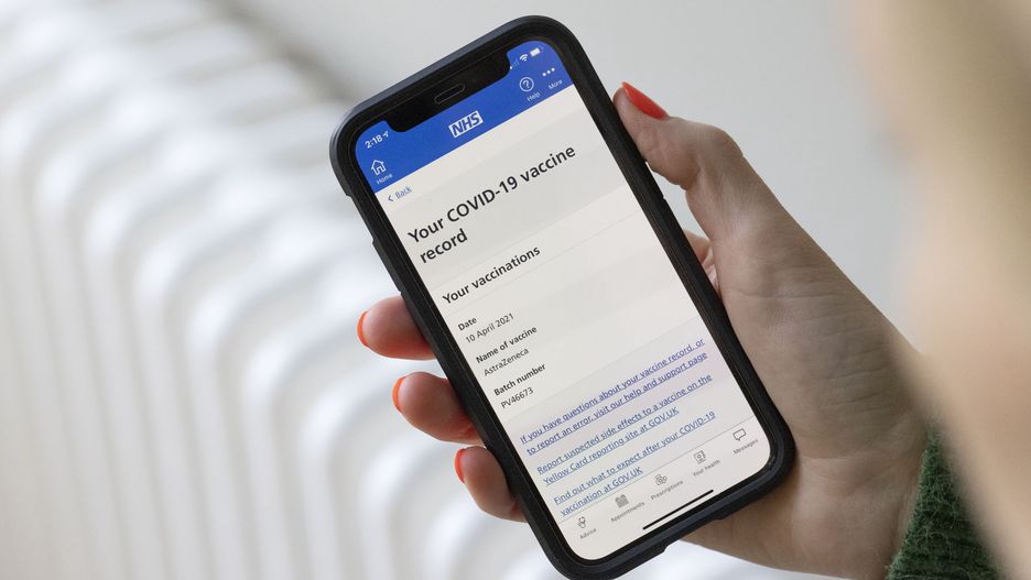 A woman uses the National Health Service (NHS) app, showing a Covid-19 vaccine record, on a smartphone arranged near Guildford, U.K., on Monday, May 17, 2021. As the bans on international travel and households mixing indoors are relaxed, the National Health Service mobile app has started showing individuals vaccine status, a key step in the development of so-called Covid passports that will be key to enabling foreign trips. Photographer: Jason Alden/Bloomberg via Getty Images