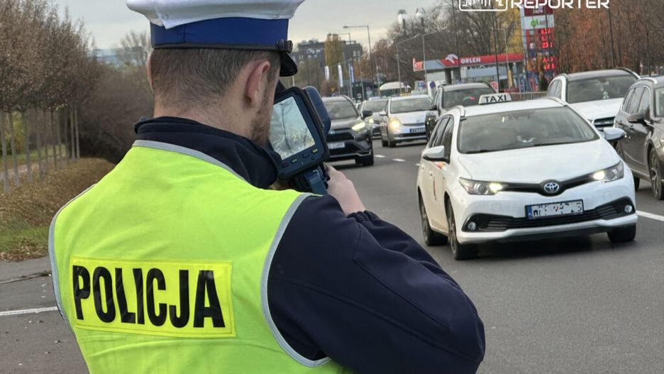 Policjant w kamizelce odblaskowej mierzy prędkość przejeżdżających samochodów na ruchliwej drodze.