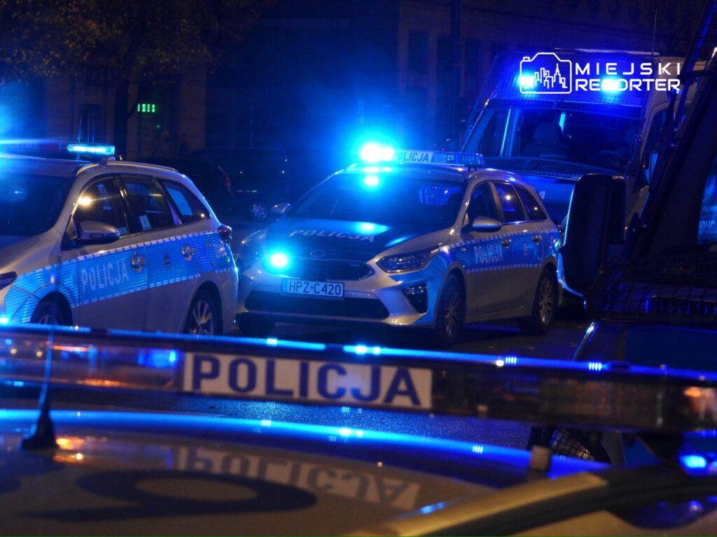 Policyjne samochody z włączonymi sygnałami świetlnymi zatrzymane na ulicy w nocy, otoczone niebieskim światłem.