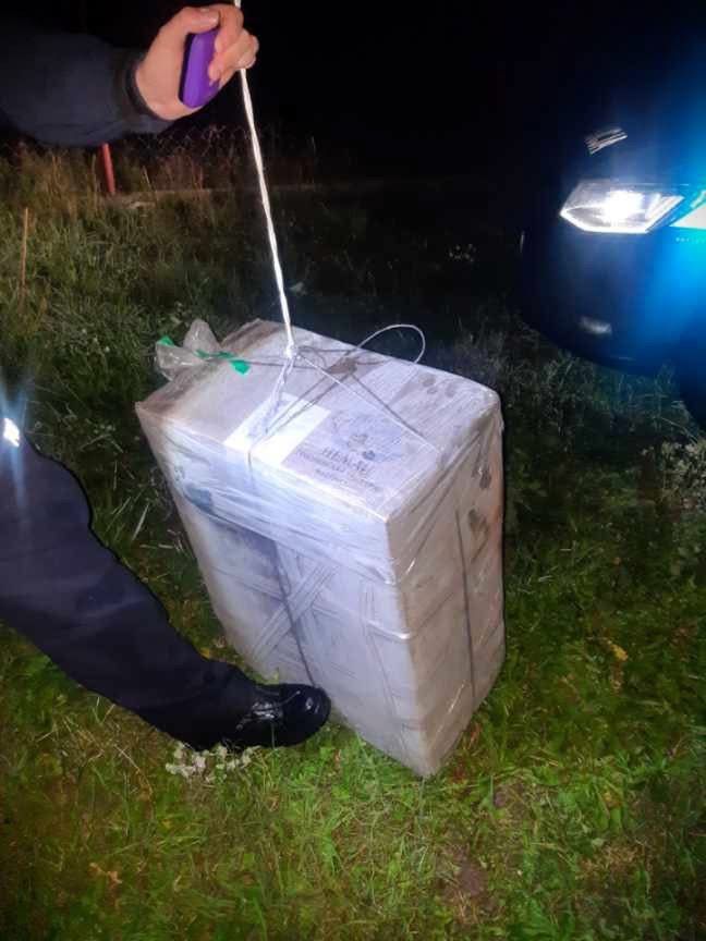 Mężczyzna w mundurze trzyma drut, przygotowując się do otwarcia paczki na trawie w nocy.