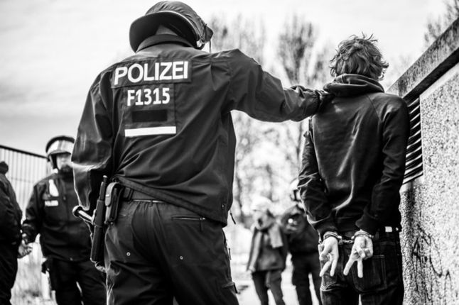 Drugie zdjęcie przedstawia zajście, które miało miejsce podczas zamieszek między zwolennikami lewicy oraz neonazistami w Berlinie. Przedstawia ono młodego chłopaka podczas aresztowania przez policję. Pokazuje on skutymi dłońmi znak zwycięstwa. Głęboki symboliczny wymiar tej fotografii daje do myślenia. By zrobić to zdjęcie Lapis musiał głęboko wejść w społeczność berlińskich zwolenników obu stron celem dowiedzenia się o tzw. „ustawkach”, gdzie po demonstracjach obu stron dochodzi do zamieszek. Tuż po zrobieniu tego zdjęcia Marek został odciągnięty przez policję i powalony na ziemię, po czym ledwo uniknął aresztowania.