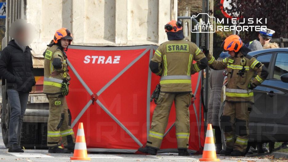 Czterej strażacy w hełmach rozmawiają przy czerwonym namiocie z napisem "STRAŻ" na poboczu drogi.