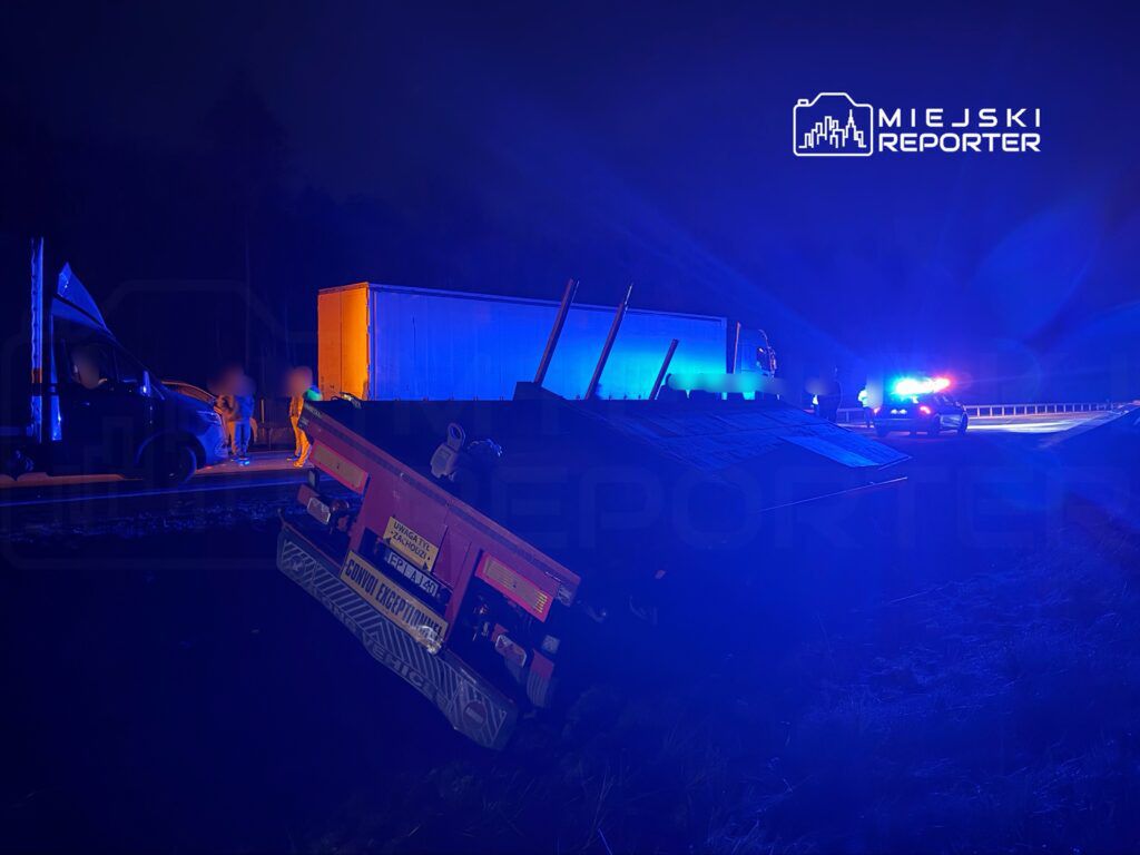 Na poboczu drogi stoi przewrócony pojazd ciężarowy, a obok niego znajdują się funkcjonariusze policji.