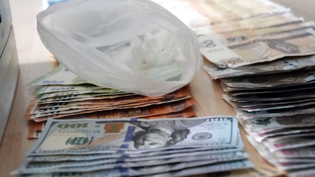 Zgrupowanie banknotów różnych walut obok plastikowej torby na drewnianym stole.