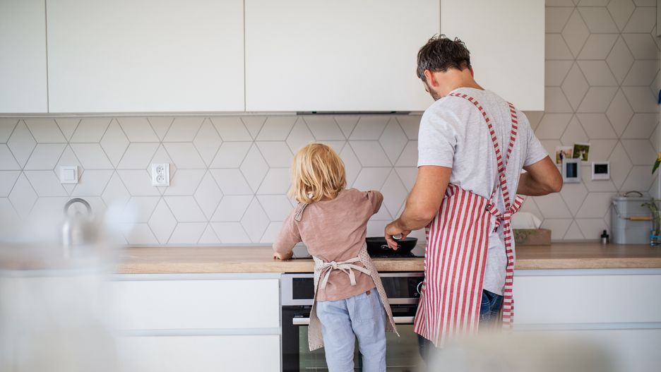 A rear view of small boy with father indoors in kitchen making pancakes.A rear view of small boy helping father indoors in kitchen with making pancakes.family, young, caucasian, man, males, father, parents, people, adults, children, kids, boy, son, small, toddler, blond, cute, beautiful, together, happy, indoors, inside, interior, flat, apartment, house, lifestyle, day, kitchen, apron, preparing, food, meal, helping, cooking, unrecognizable, pan, frying, stove, rear, view, back, striped, red, white, standing, family, young, caucasian, man, males, father, parents, people, adults, children, kids, boy, son, small, toddler, blond, cute, beautiful, together, happy, indoors, inside, interior, flat, apartment, house, lifestyle, day, kitchen, apron, preparing, food, meal, helping, cooking, unrecognizable, pan, frying, stove, rear, view, back, striped, red, white, standing