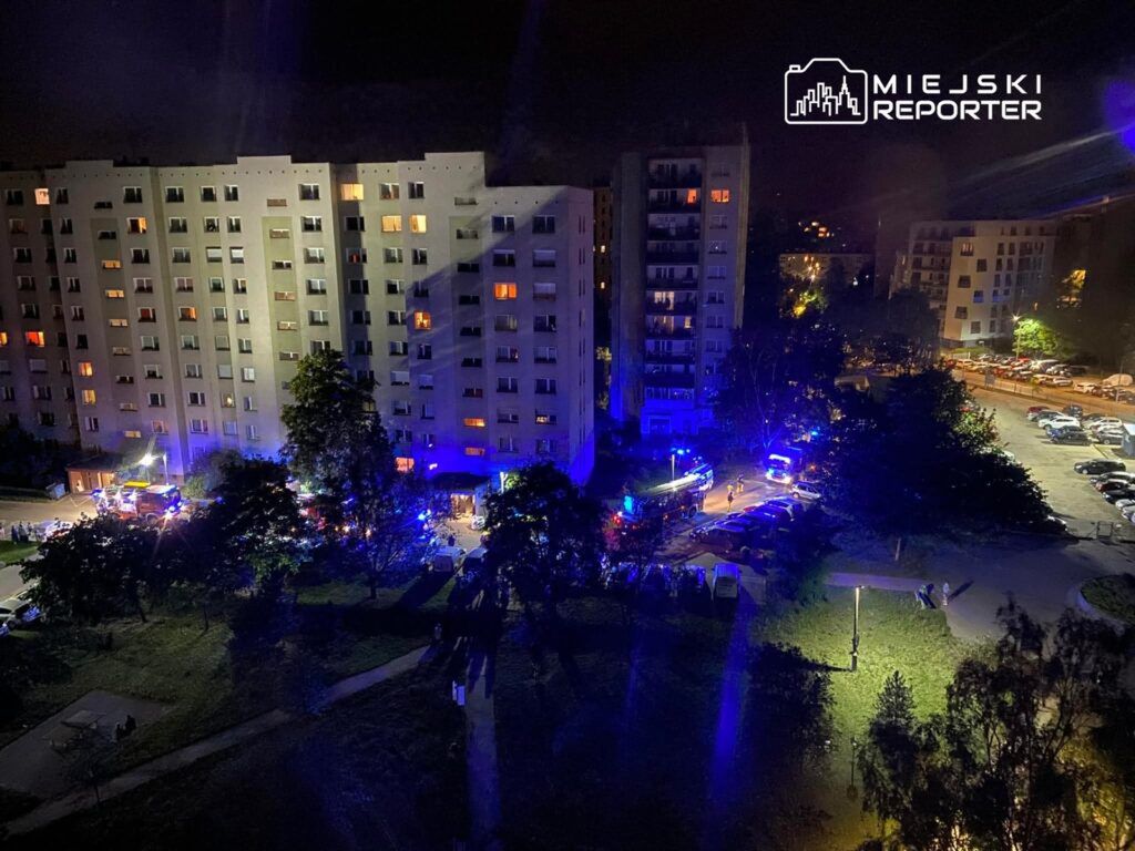 W nocy przed budynkiem mieszkalnym z niebieskimi i czerwonymi światłami interwencyjnymi zgromadziły się służby ratunkowe.