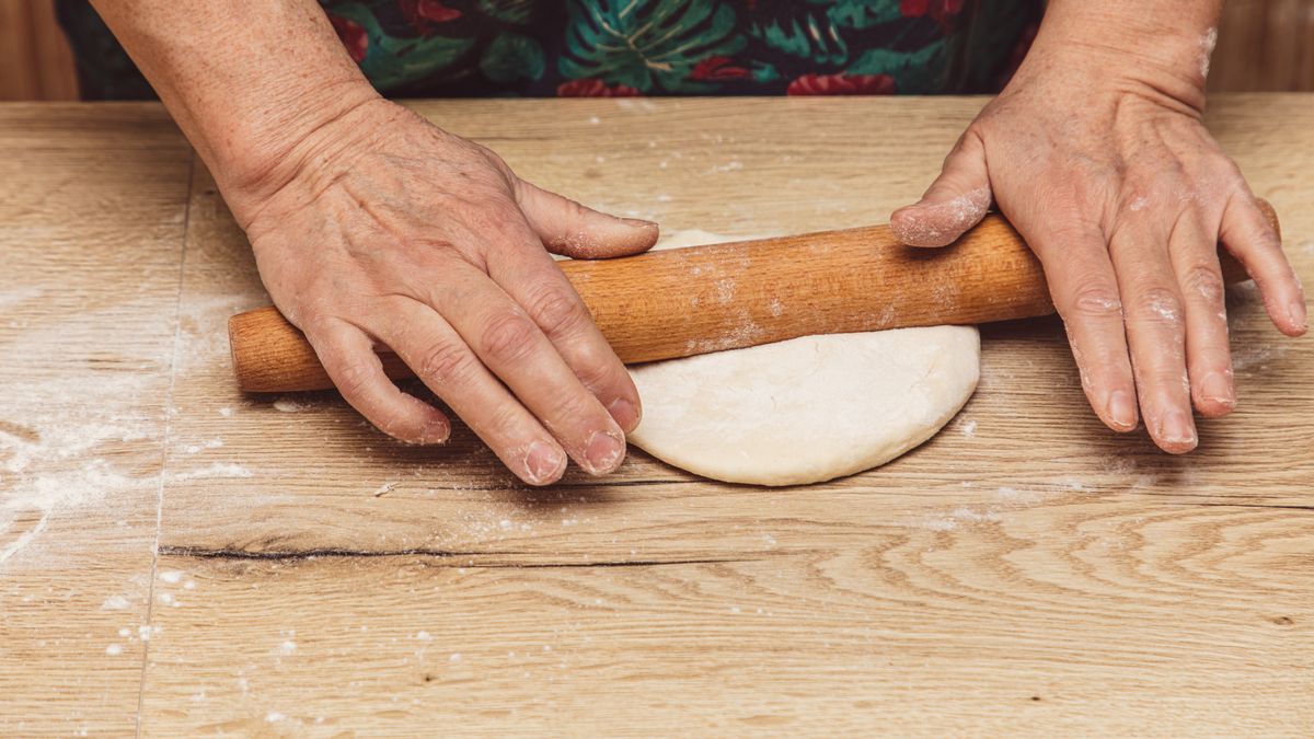 Starsza kobieta wałkuje ciasto pierogowe