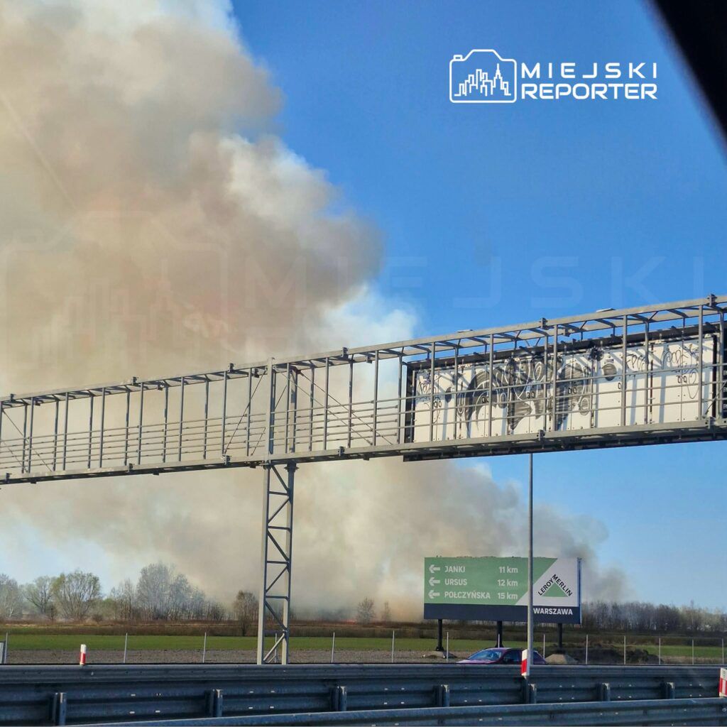 Gęsty dym unosi się nad polem w pobliżu drogi, z widocznym znakiem kierunkowym do Janków i Ursusa.