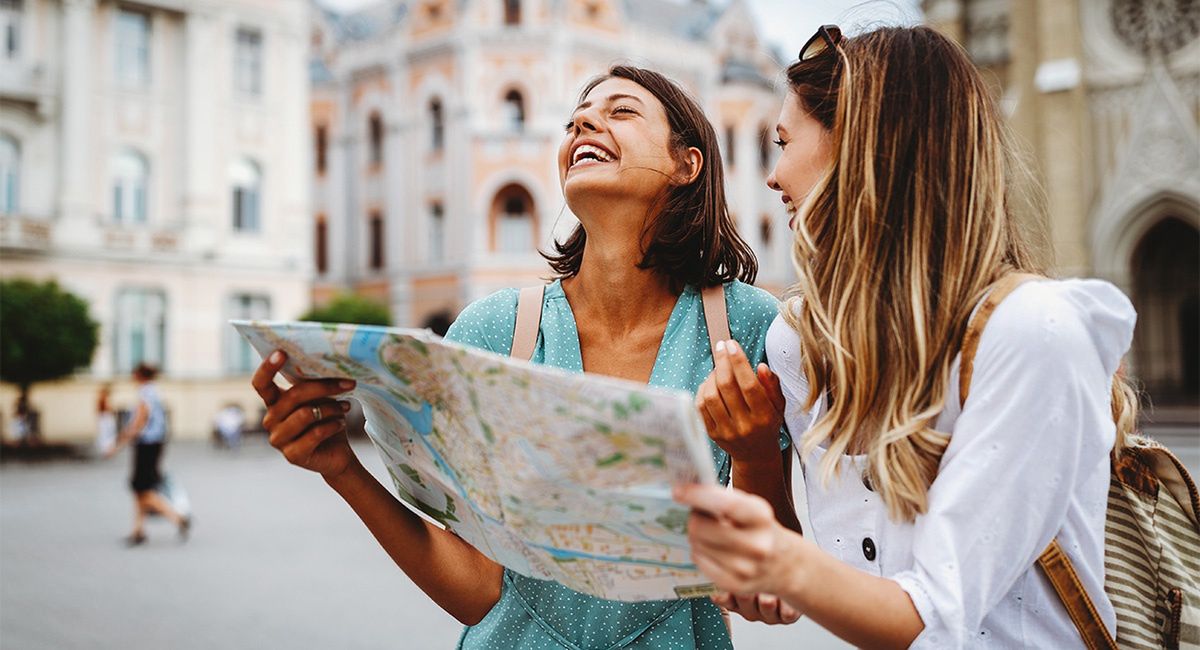 Szczęśliwe młode kobiety zwiedzają nowe miejsca z mapą 