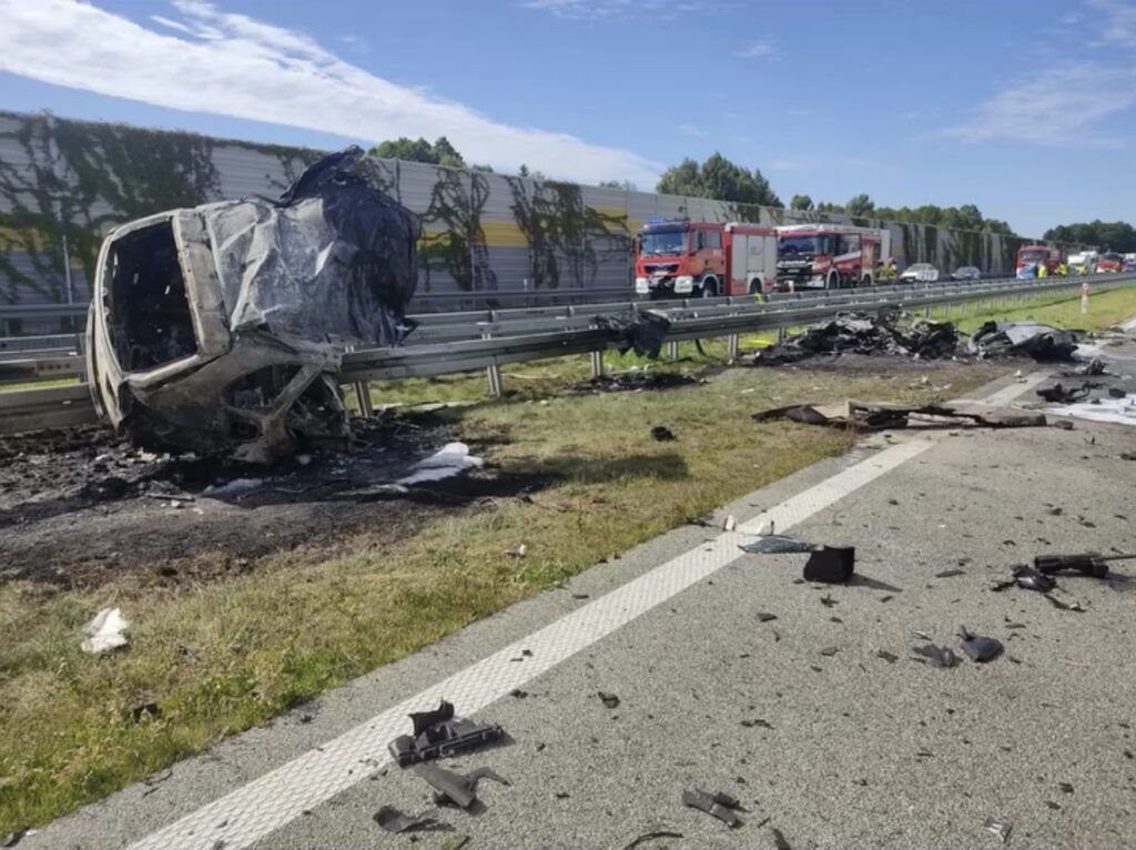 Zniszczony samochód leży na poboczu drogi, obok znajdują się resztki wraku i sprzęt strażacki.