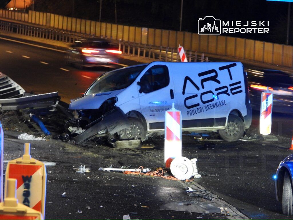 Wielka biała furgonetka z napisem "ART CORE" uderzyła w barierkę na autostradzie, wokół leżą resztki wraku.