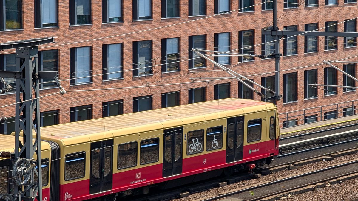 A Berlin S-Bahn suburban train runs along elevated tracks beside a modern office building in Berlin, Germany, on July 19, 2025. The red and yellow carriage features bicycle and wheelchair symbols on its exterior. (Photo by Michael Nguyen/NurPhoto via Getty Images)