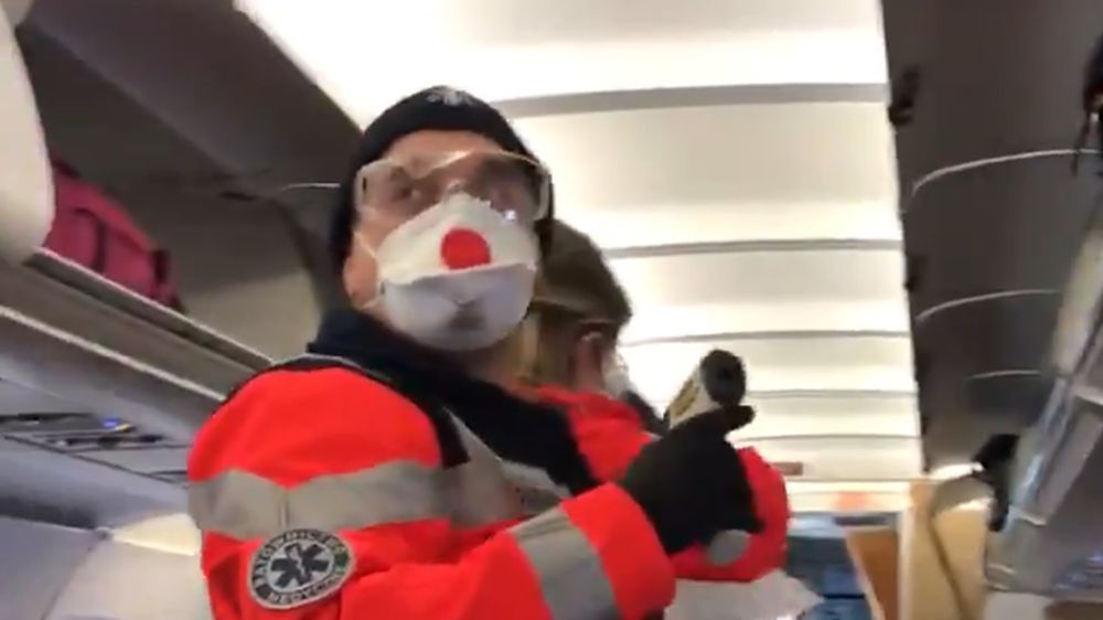 ratownik medyczny mierzący temperaturę pasażerom samolotu z Włoch