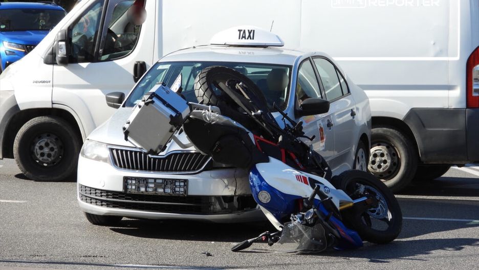 Zniszczony motocykl leży na dachu obok uszkodzonego samochodu osobowego na ruchliwej ulicy.