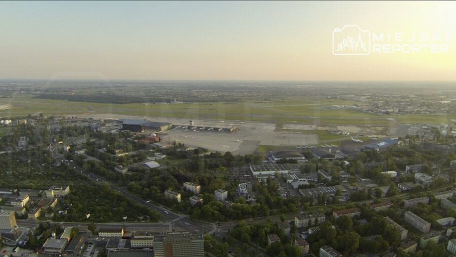Widok na lotnisko z pasami startowymi i terminalami, otoczone zielenią i zabudową miejską.
