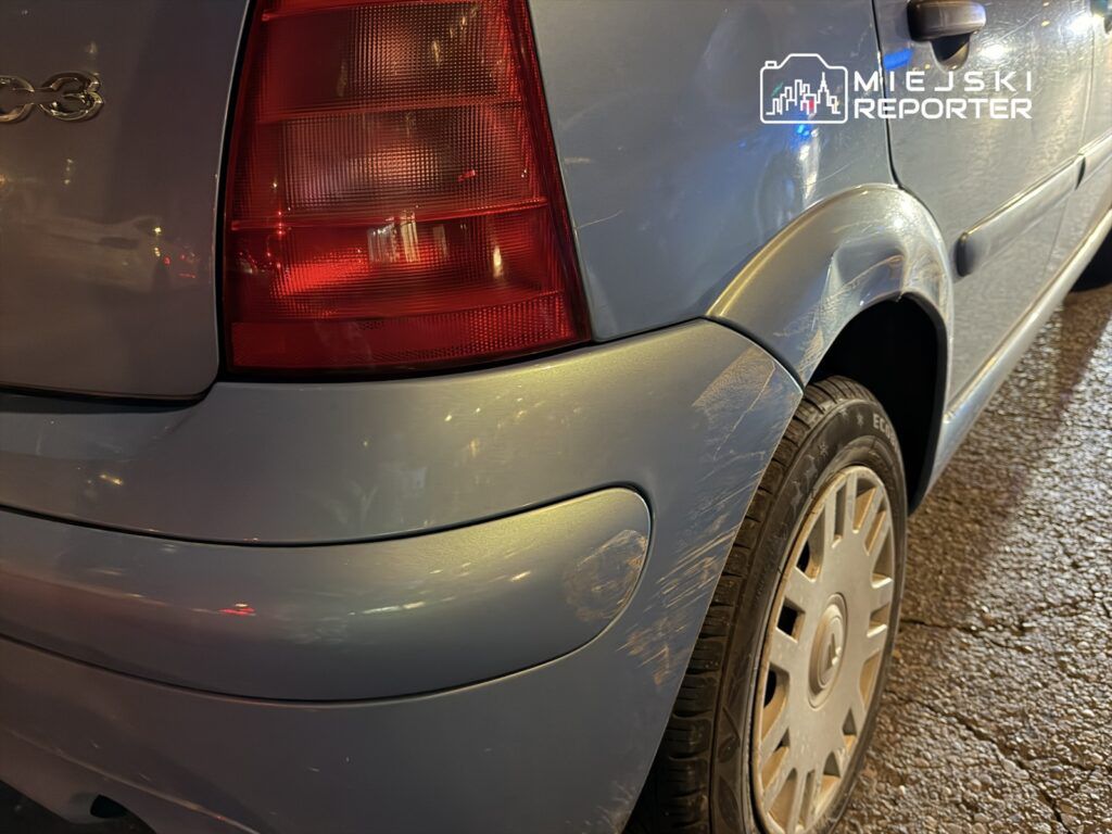 Zarysowany tylny błotnik niebieskiego samochodu osobowego zaparkowanego na oświetlonej ulicy.