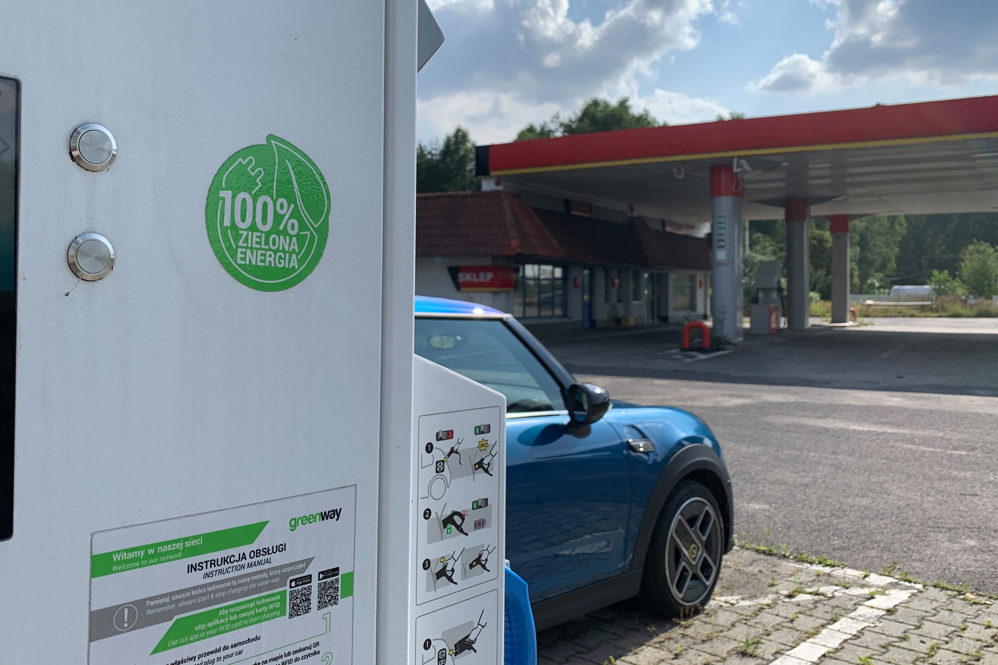 Wymowne zdjęcie – elektryk ładuje się zieloną energią na terenie zamkniętej stacji paliw