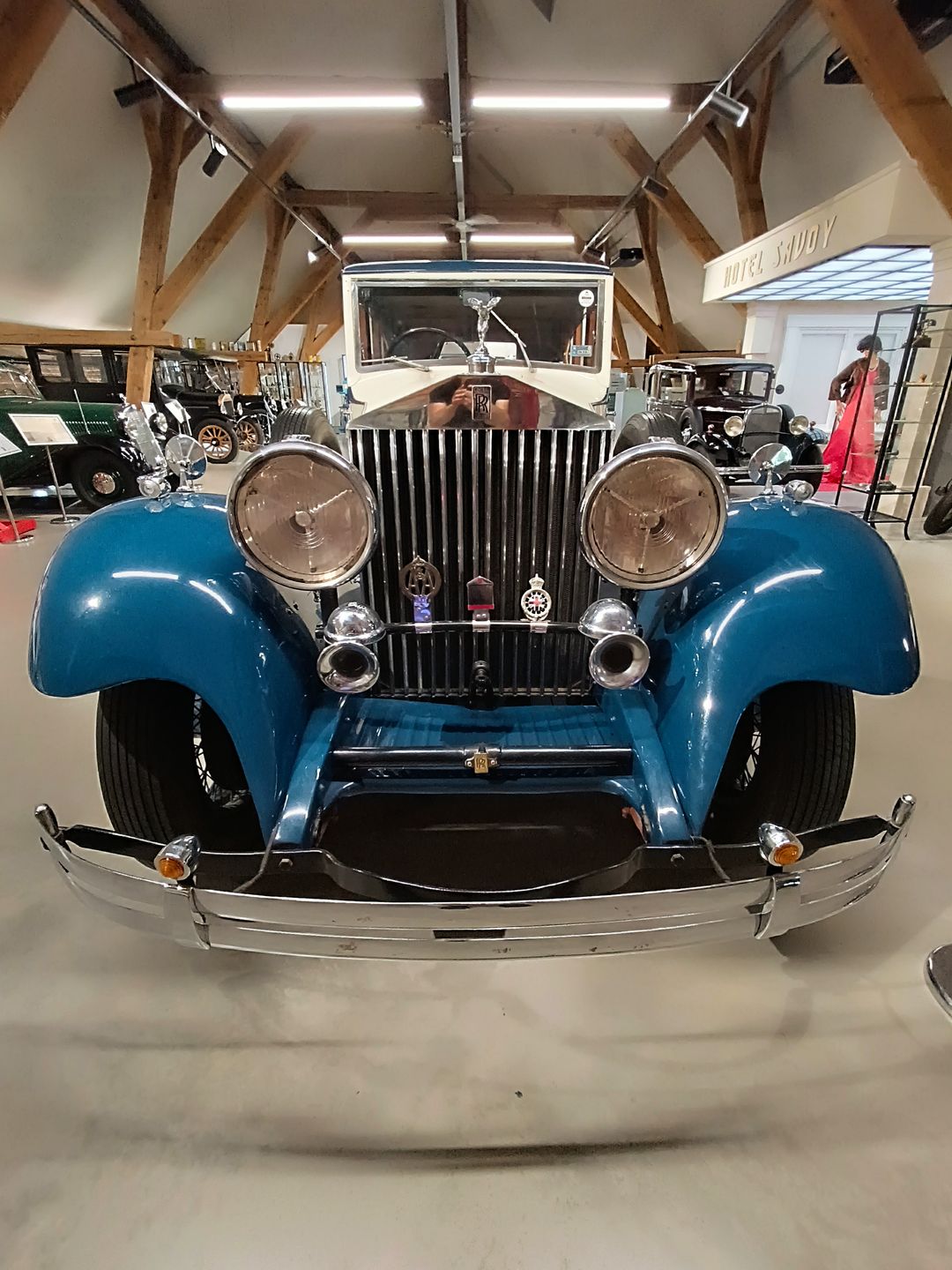 Przód zabytkowego Rolls-Royce’a: niebieskie błotniki, pionowa chłodnica, okrągłe reflektory i figurka nad znakiem marki