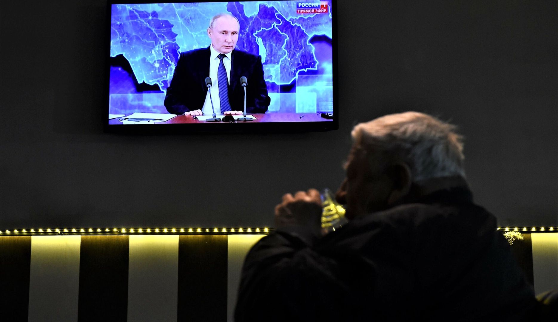 Mężczyźni piją wódkę w barze w Sankt Petersburgu. Na ekranie TV Władimir Putin podczas corocznej konferencji prasowej transmitowanej na propagandowym kanale Rossija 24
