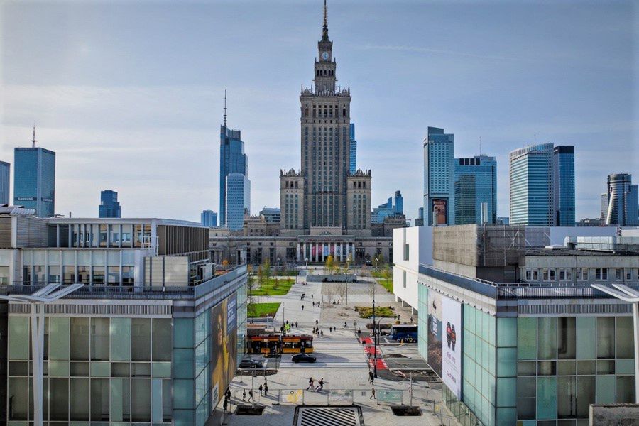 Widok na nowoczesne biurowce otaczające Pałac Kultury i Nauki w Warszawie, w tle jasne niebo.