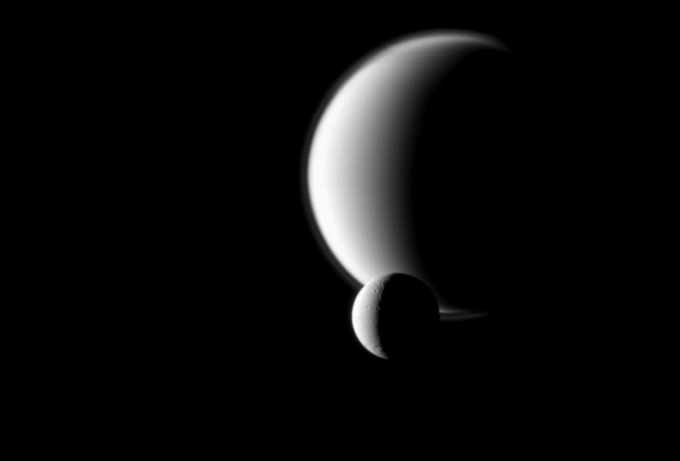Poznaczona kraterami Dione na tle wiecznie zachmurzonego Tytana. Odkrywcą tej pierwszej był wspomniany już Giovanni Cassini. Tytana odkrył nieco wcześniej holenderski matematyk, fizyk, horolog i astronom Christiaan Huygens. Jego nazwisko nosił próbnik opuszczony przez sondę Cassini na powierzchnię Tytana na przełomie lat 2004/5.