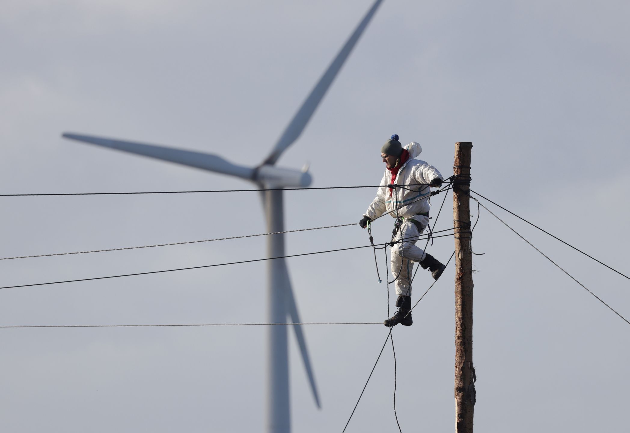 ERKELENZ, GERMANY - JANUARY 11: An activist stands on a rope on a pole as a wind turbine spins behind at the settlement of Luetzerath next to the Garzweiler II open cast coal mine on January 11, 2023 near Erkelenz, Germany. Police are evicting environmental activists who have occupied the abandoned Luetzerath settlement and are seeking to prevent Luetzerath's demolition that will make way for an expansion of the Garzweiler coal mine. The North Rhine-Westphalia state government of German Christian Democrats (CDU) and Greens has approved the demolition and the coal mine expansion, while at the same time announcing an accelerated phase out of coal-fired energy production in the state of North Rhine-Westphalia from 2038 to 2030. Other nearby settlements that were also slated for demolition will now be spared, though critics point out that Germany has sufficient energy production capacity and does not need the coal lying beneath Luetzerath. (Photo by Sean Gallup/Getty Images)