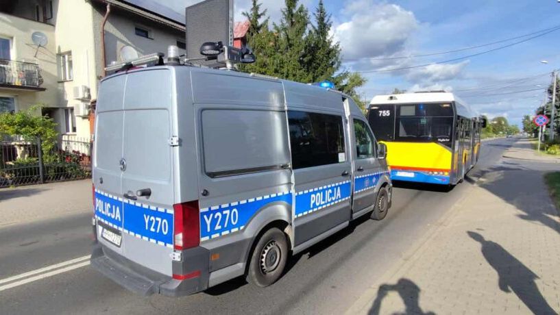 Radiowóz policyjny zatrzymany na poboczu drogi obok autobusu miejskiego w słoneczny dzień.