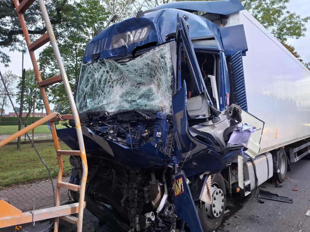 Zniszczona kabina niebieskiego tira z rozbitą szybą, stojącego na poboczu drogi, obok drabina.