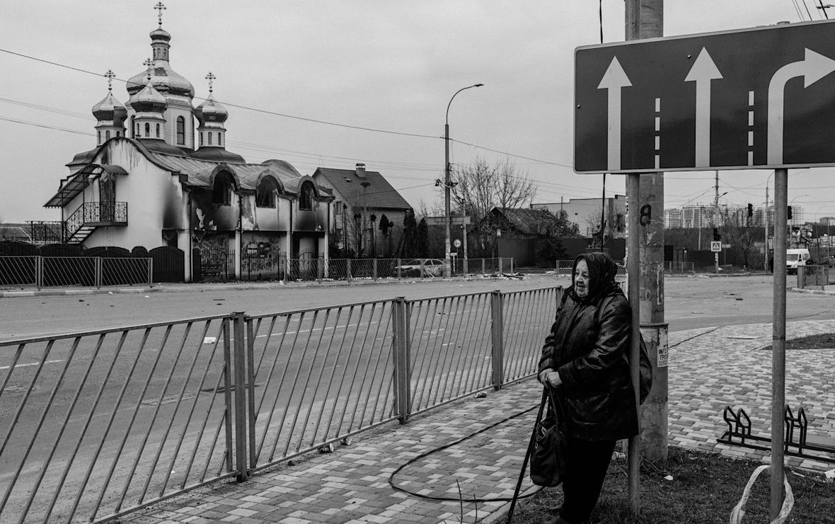 Staruszka odpoczywa po "bezpiecznej" stronie mostu. W tle  ostrzelana cerkiew