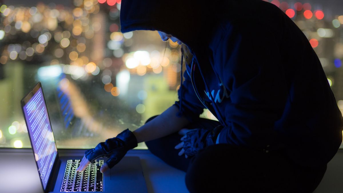 Woman in hooded sweater operating PC in dark with city in background
Benjamin Torode