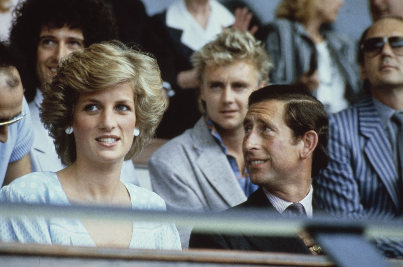 British Royals Diana, Princess of Wales, wearing a dress designed by Dale 'Kanga' Tryon, with her husband Charles, Prince of Wales, during the Live Aid concert at Wembley Stadium in London, England, 13th July 1985. Behind the Royal couple are Queen musicians, guitarist Brian May and drummer Roger Taylor. (Photo by Fox/Keystone/Hulton Archive/Getty Images)