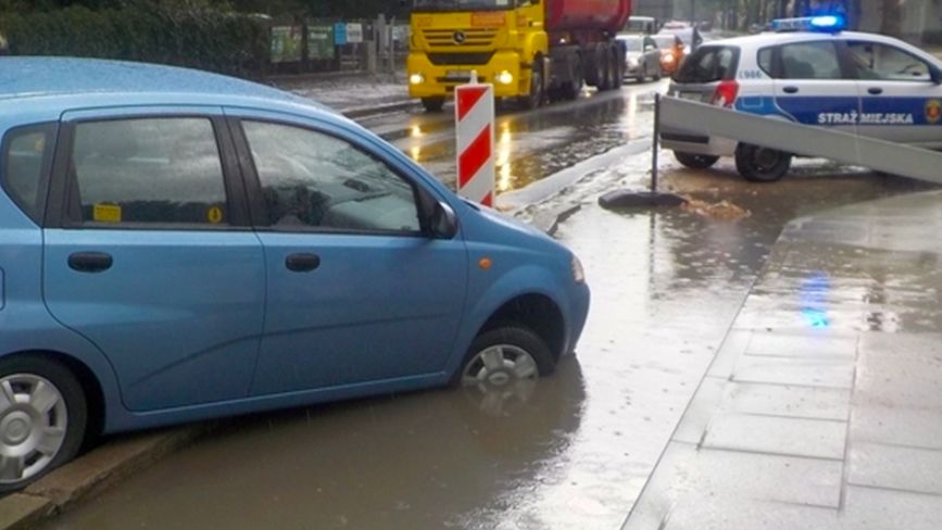 Warszawa. Chevrolet w wielkiej kałuży. Kierująca wykonała niefortunny manewr. Wydostać się z tej opresji pomogli jej strażnicy miejscy (Stołeczna Straż Miejska)