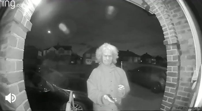 Starsza kobieta z nożem uchwycona przez kamerę przed drzwiami.