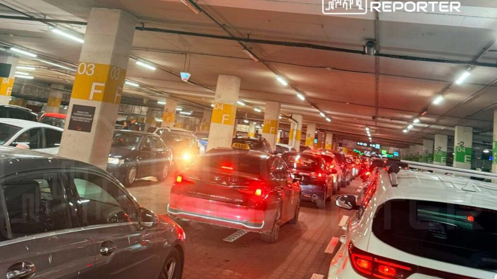 Ruch samochodów w zatłoczonym parkingu podziemnym, z widocznymi światłami hamowania i oznaczeniami miejsc.