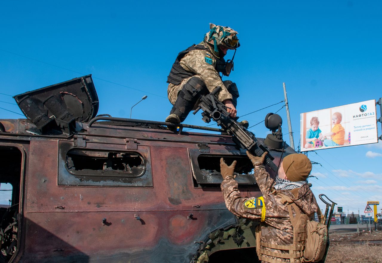 27 lutego 2022, Ukraina, Charków: Żołnierze w pobliżu spalonego rosyjskiego AFV "Tygrys" w Charkowie.