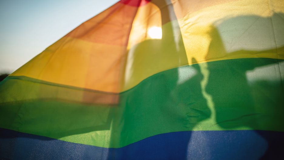 Lesbian women kissing behind the rainbow flag