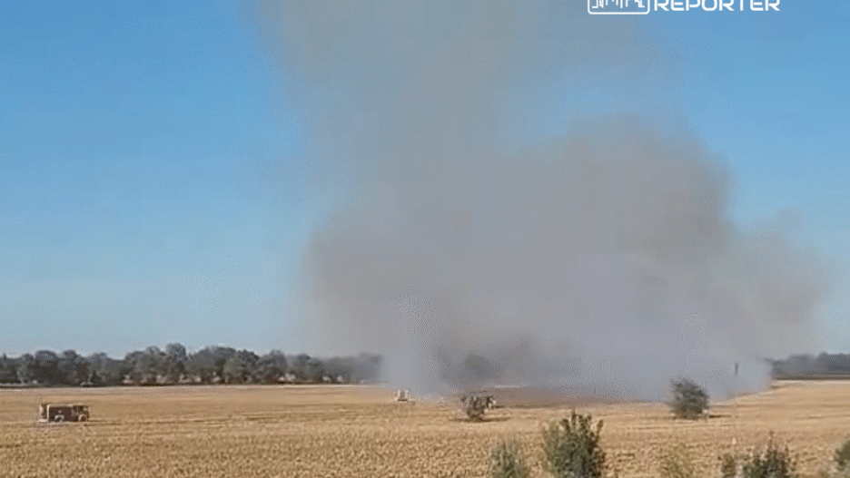 Dym unoszący się nad polem zbożowym, w tle widoczne maszyny rolnicze pracujące na polu.