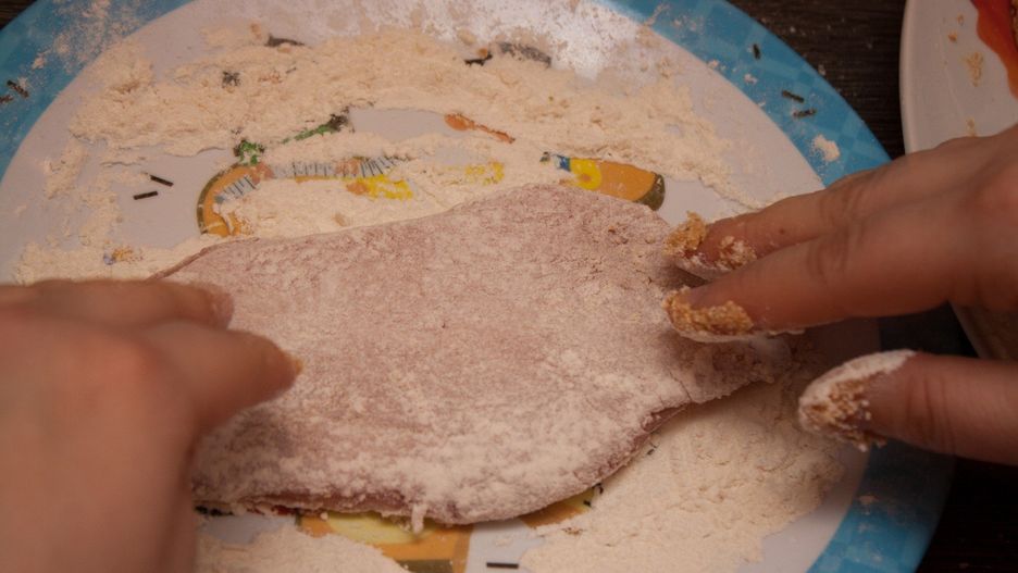 Two hands putting flour on meat making a wiener schnitzel