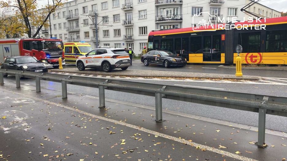 Na ulicy stoją pojazdy ratunkowe, w tym wóz strażacki i karetka, otoczone przez samochody osobowe.