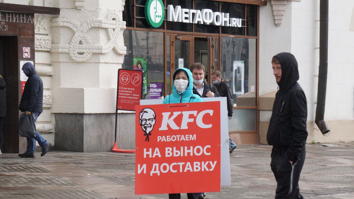MOSCOW, RUSSIA - MAY 19: (RUSSIA OUT) A woman in a protective mask carries a billboard of the KFC restaurant on May 19, 2020 in Central Moscow, Russia. Thousands of people went back to work Monday as Russia is gradually easing the quarantine measures. (Photo by Mikhail Svetlov/Getty Images)