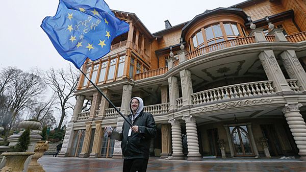 Mężczyzna z flagą UE przed budynkiem rezydencji Wiktora Janukowycza