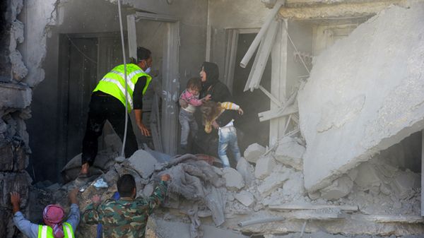 Ratownicy ewakuują kobietę z dwójką dzieci z budynku zbombardowanego przez reżimowe lotnictwo