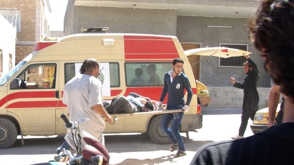 Mężczyźni niosą rannego podczas ostrzału do ambulansu; Idlib