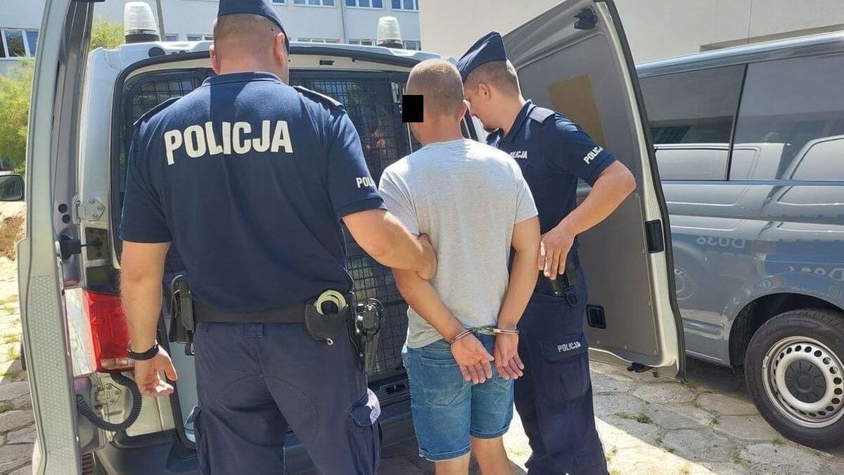 Mężczyzna z kajdankami na rękach prowadzony do radiowozu