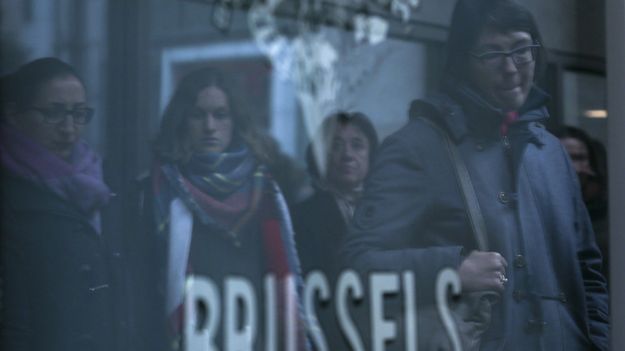 Ludzie odbijają się w szybie podczas minuty ciszy w Brukseli