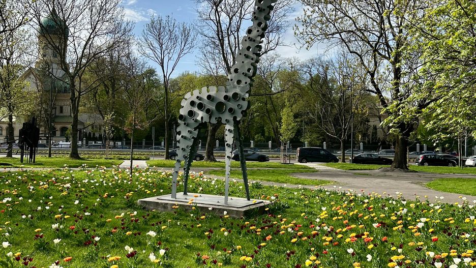 giraffe sculpture, metal statue, tulips, flowerbed, park, public art, spring flowers, sunny day, blue sky, outdoor, decorative animal, urban nature, colorful, city park, warsaw, poland