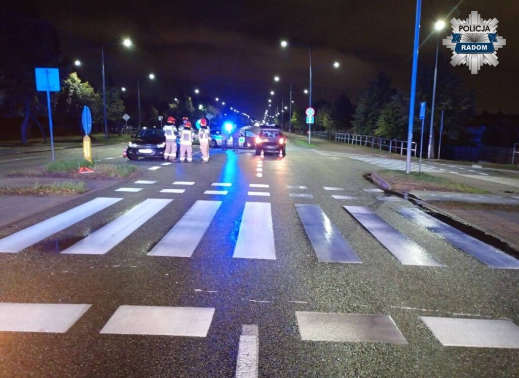 Grupa ratowników w odblaskowych kamizelkach pracuje przy wypadku drogowym na ulicy z oświetleniem nocnym.