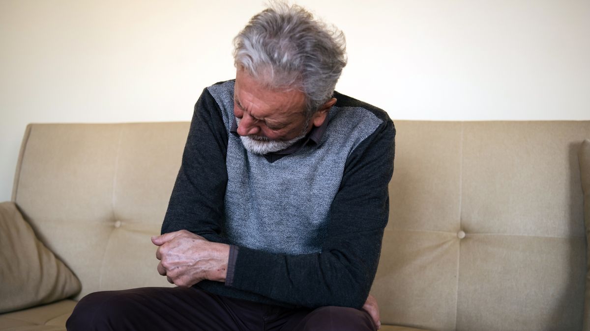 Senior man with a pain in the elbowPhoto of a senior man feeling insufferable pain in the elbow. An elderly man is lying on the sofa at home and holding his elbow due to hard pain.RealPeopleGroup