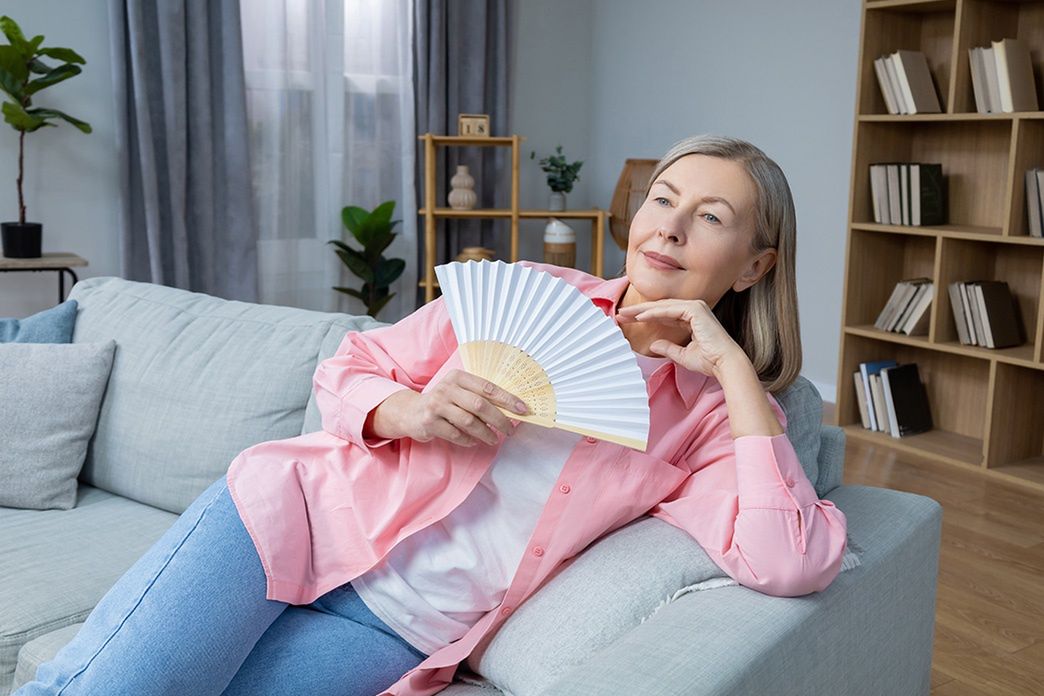 Kobieta w różowej koszuli leży na kanapie i wachluje się papierowym wachlarzem w salonie. - zdjęcie